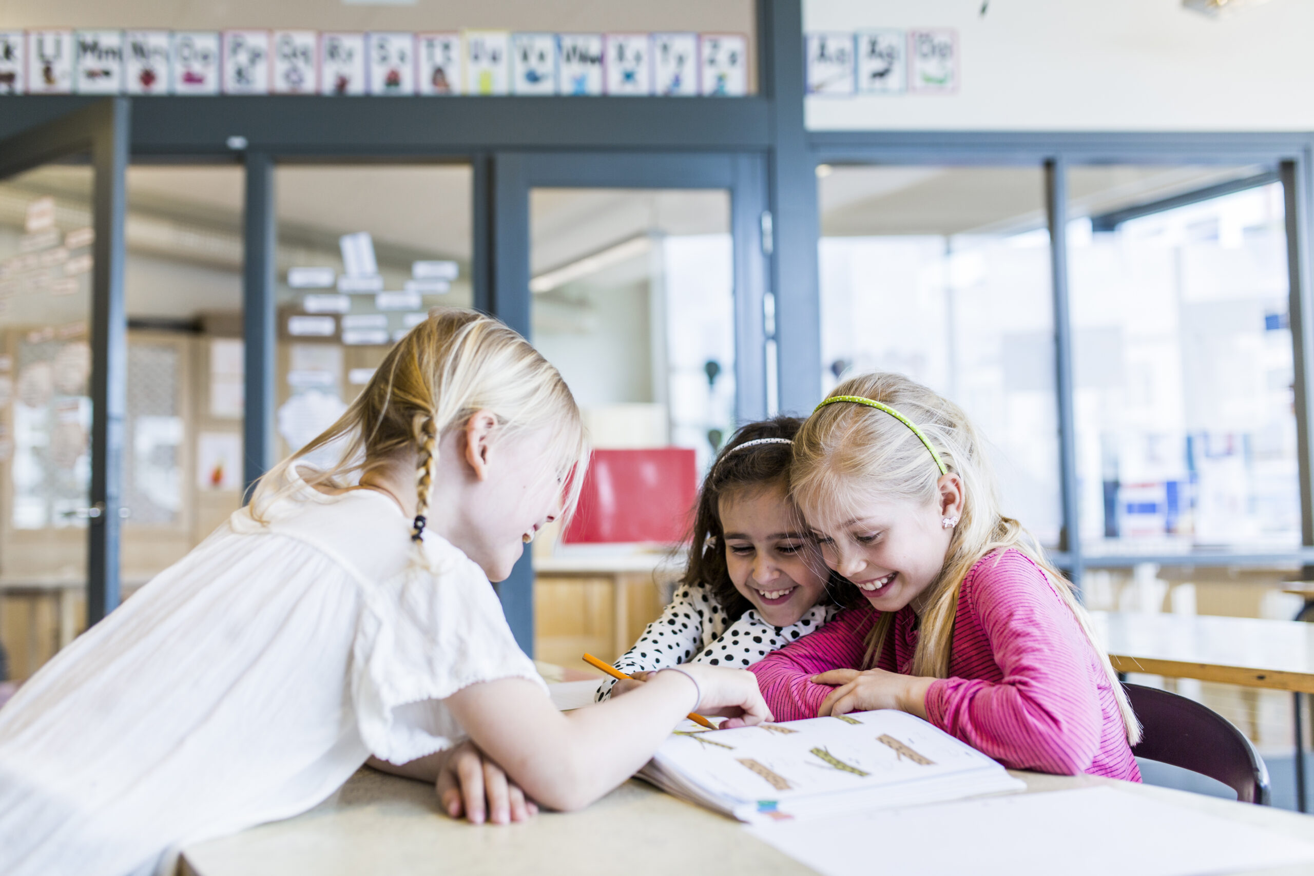 Niñas en primaria leyendo juntas y sonriendo en el aula
