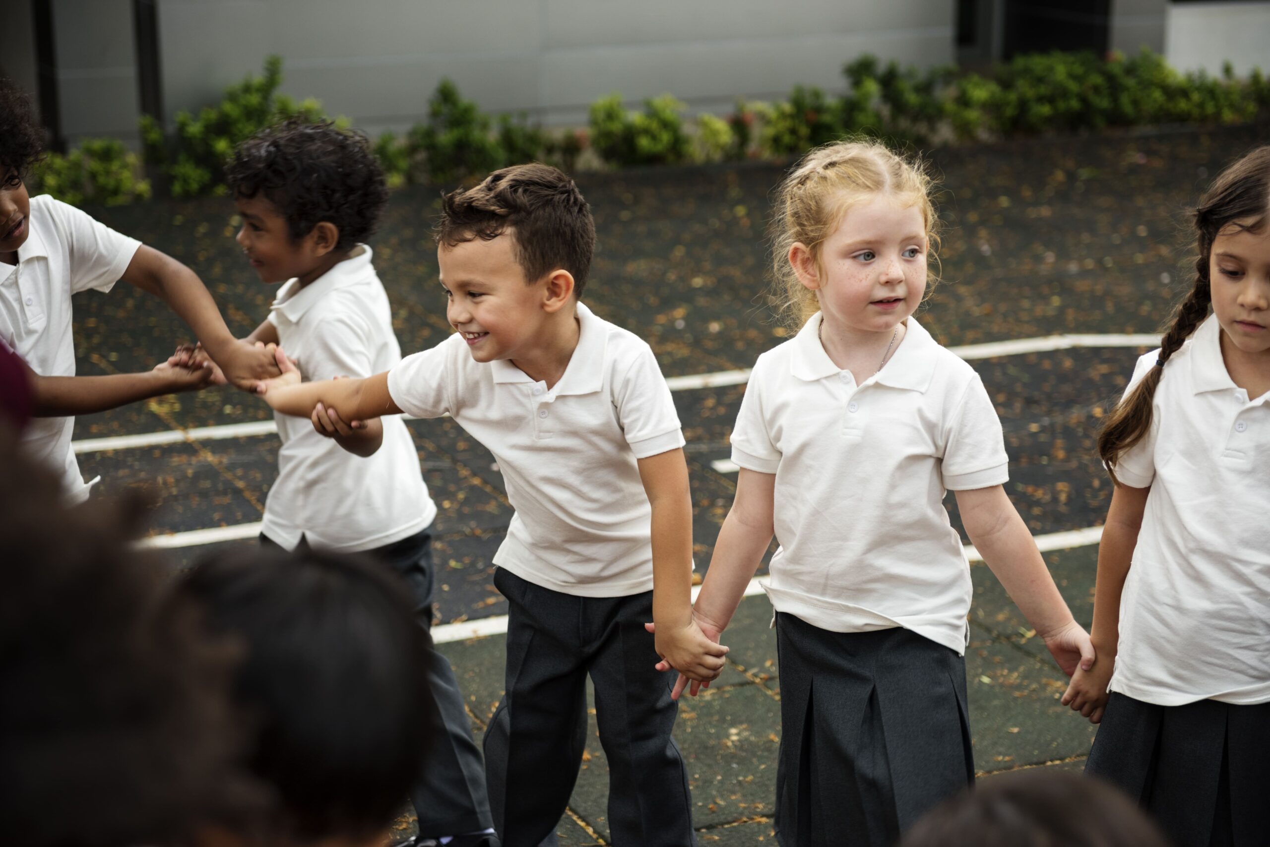 Niños de educación infantil cogidos de la mano en el patio del colegio, aprendiendo valores como el respeto y la convivencia desde pequeños.