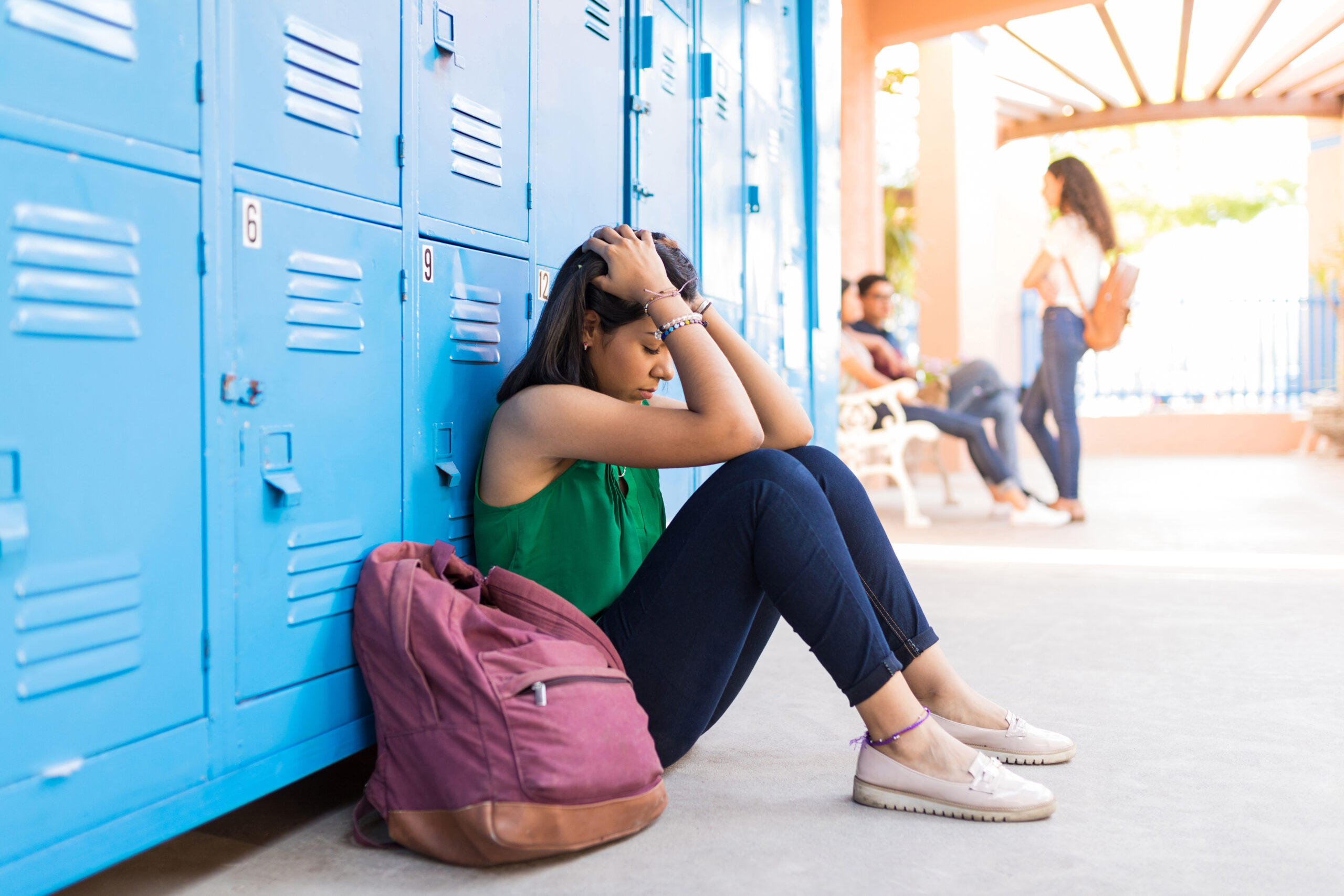 Adolescente sentada en el suelo del colegio mostrando señales de malestar emocional y aislamiento